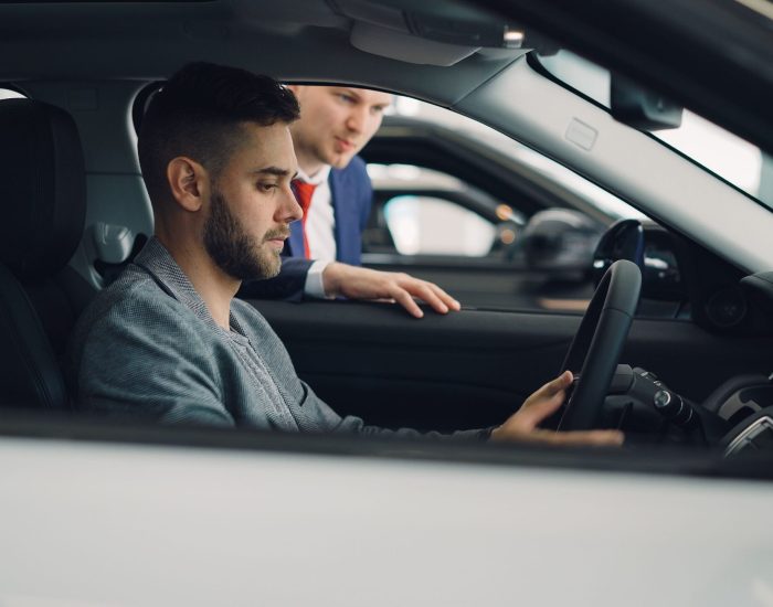 Man examining car interior with salesman at a dealership, highlighting car features.