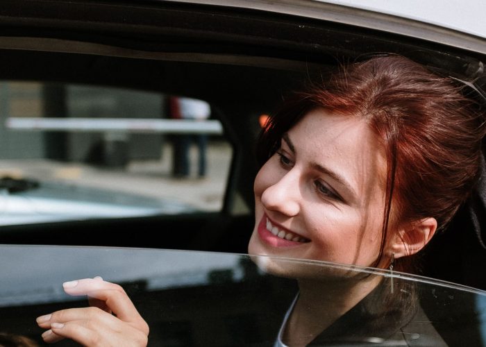 A cheerful woman smiles from the backseat of a moving taxi, city street view.